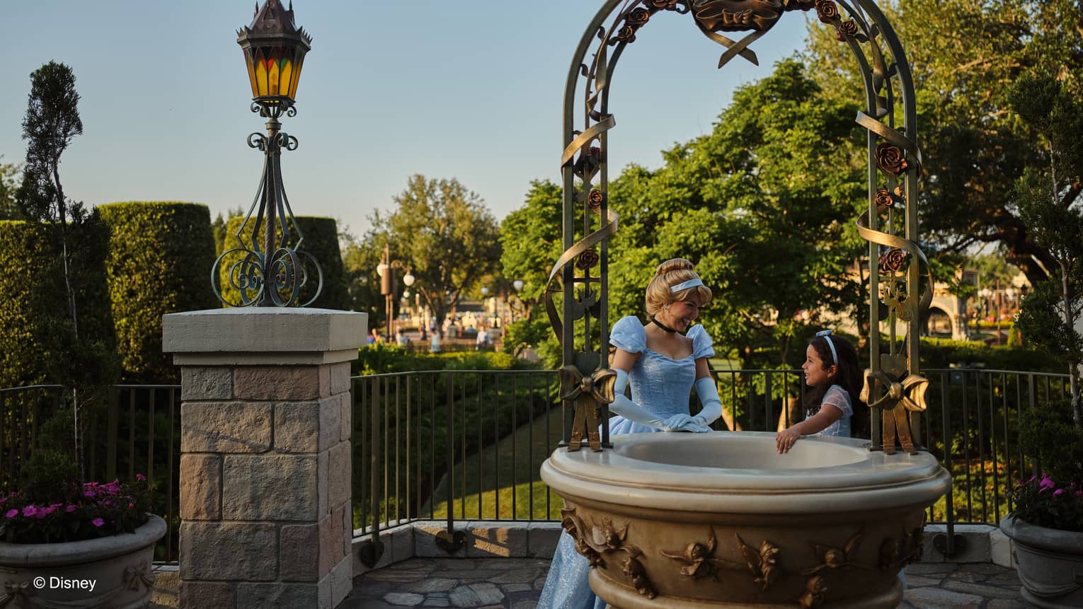 Character dressed as Cinderella stand with a child dressed as Cinderella around a fountain