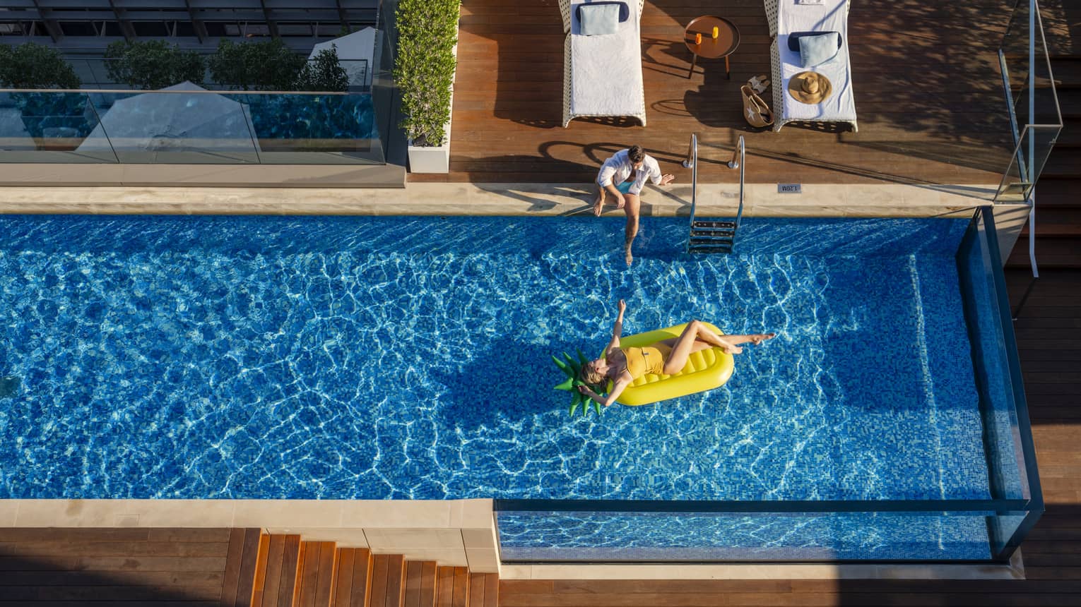 Woman lays on yellow floatie in pool, situated on top of building