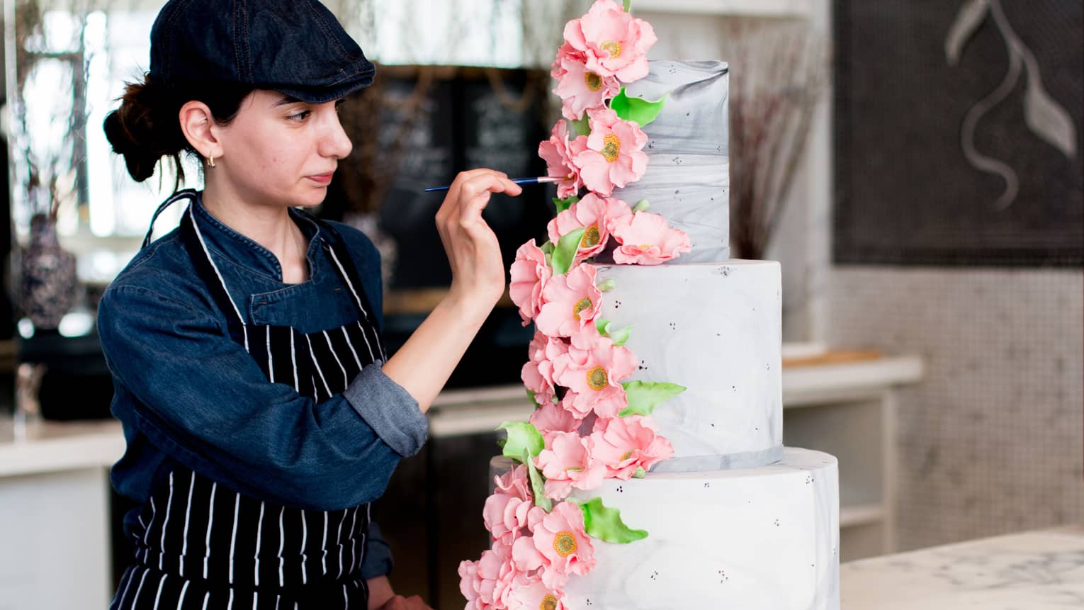 Chef places large pink flowers on three tiered wedding cake