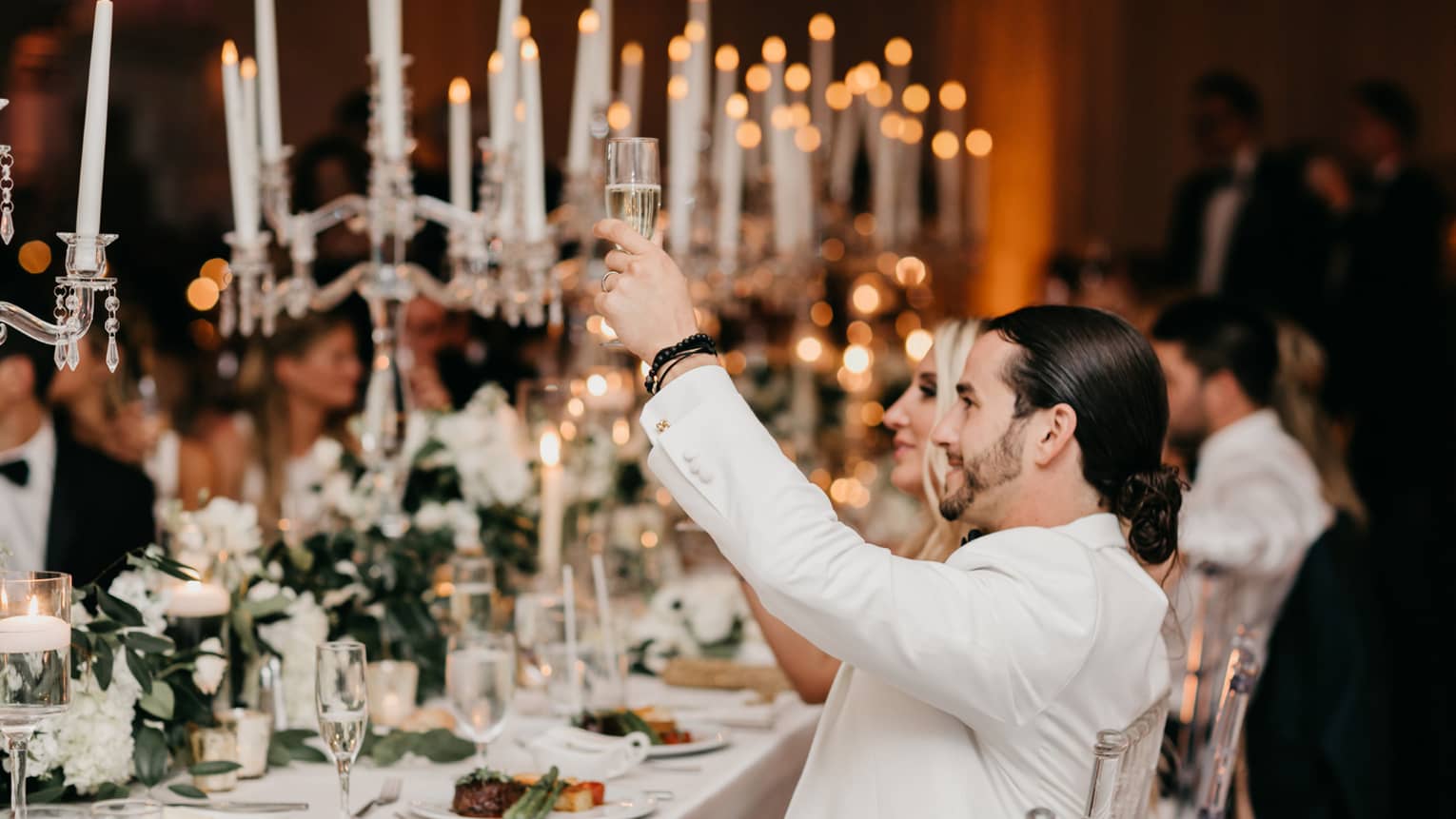 Wedding guests raise glasses during toast at candlelit banquet table