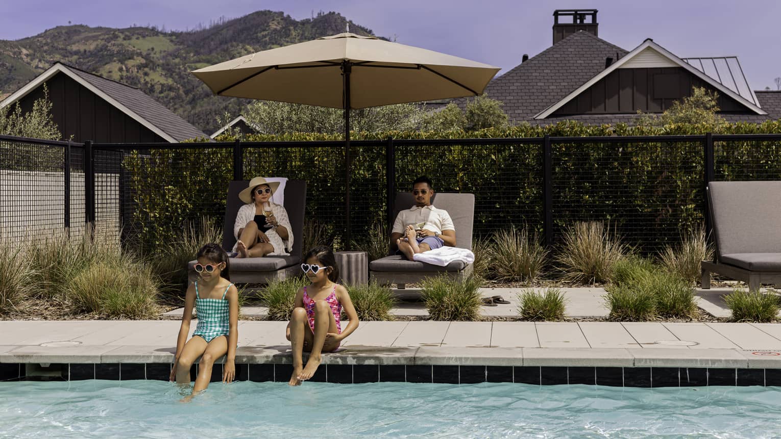 Two guests sitting on lounge chairs while the other two guests sit near the pool.