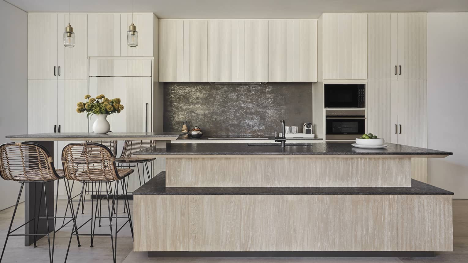 Modern kitchen with light wood cabinets, wooden island, four high-top rattan chairs