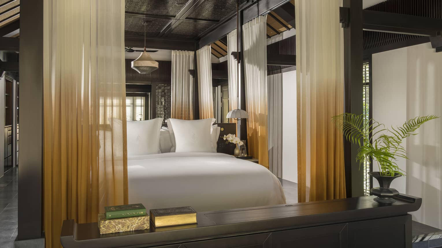 A resort bedroom featuring a king bed with orange and white curtains lining a four-post bed