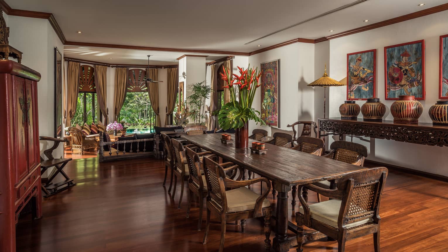 Long wood dining table with vase with tall tropical flowers in bright room