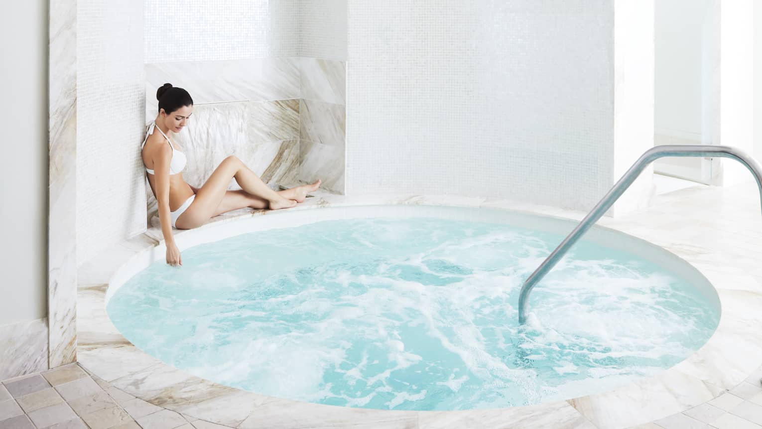 A woman relaxes by a marble hot tub in the spa