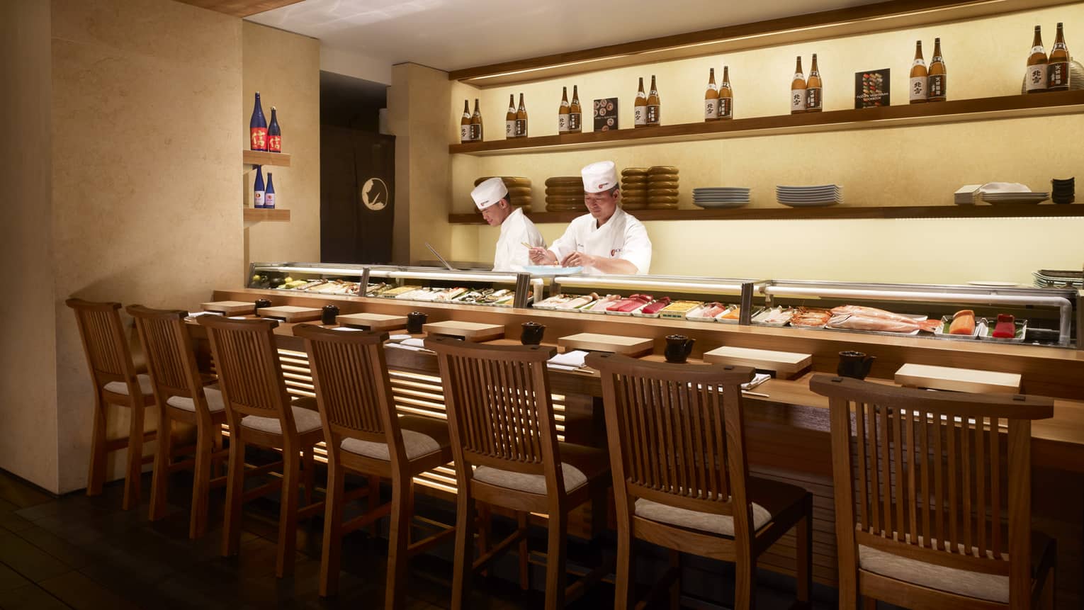 Two sushi chefs behind small glass counter filled with fresh raw fish filets, whole fish