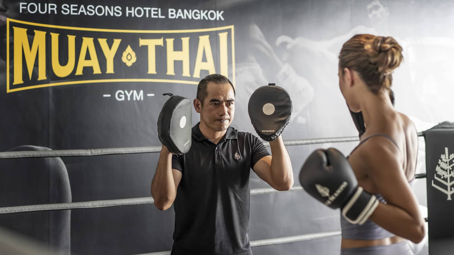 Woman practices Muay Thai with instructor in the ring of a gym