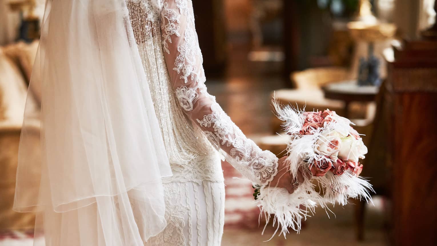 A close up of a bride's bouquet made up of white roses, pink flowers and white feathers