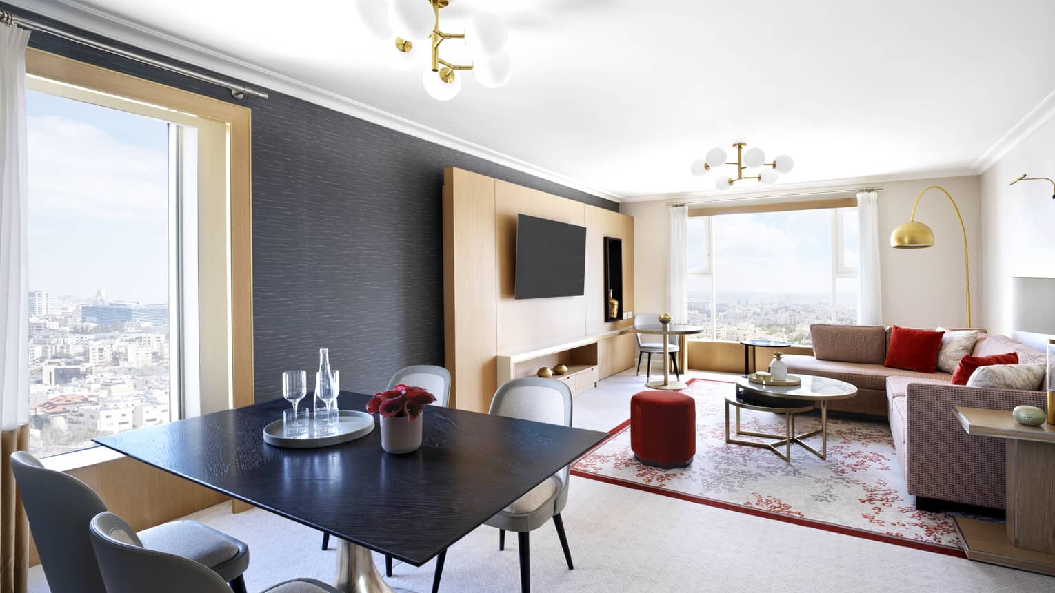 A spacious parlour with a small seating area, and an L-shaped couch all overlooking the city. 