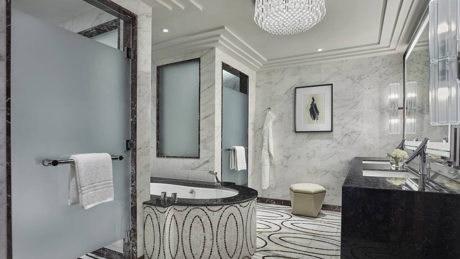 Elegant marble bathroom with a soaking tub, black granite vanity, frosted glass shower doors and intricate patterned flooring, accented by soft lighting