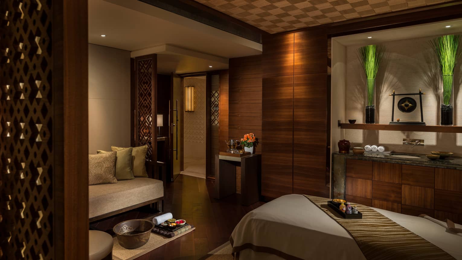Spa treatment room with carved wood detail walls, bed and table with trays with oils