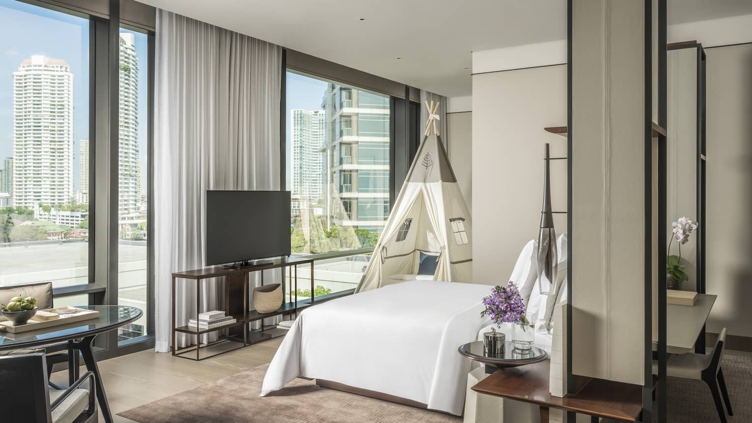 Hotel room with king bed, wall of windows, and kids teepee