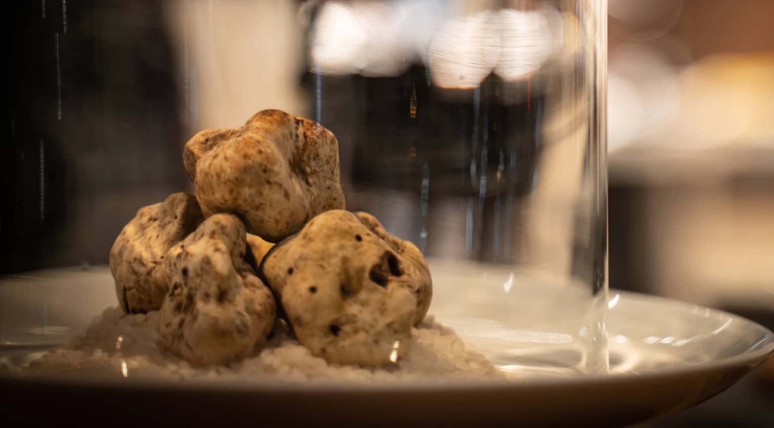 Three irregular truffles stacked on a white plate under a cloche