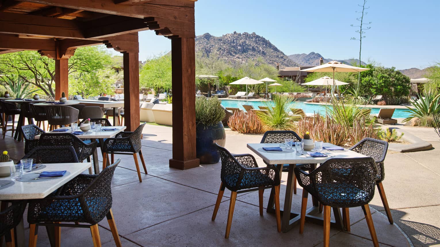 Outdoor patio with table and chairs, view of the pool, and mountains in the background.