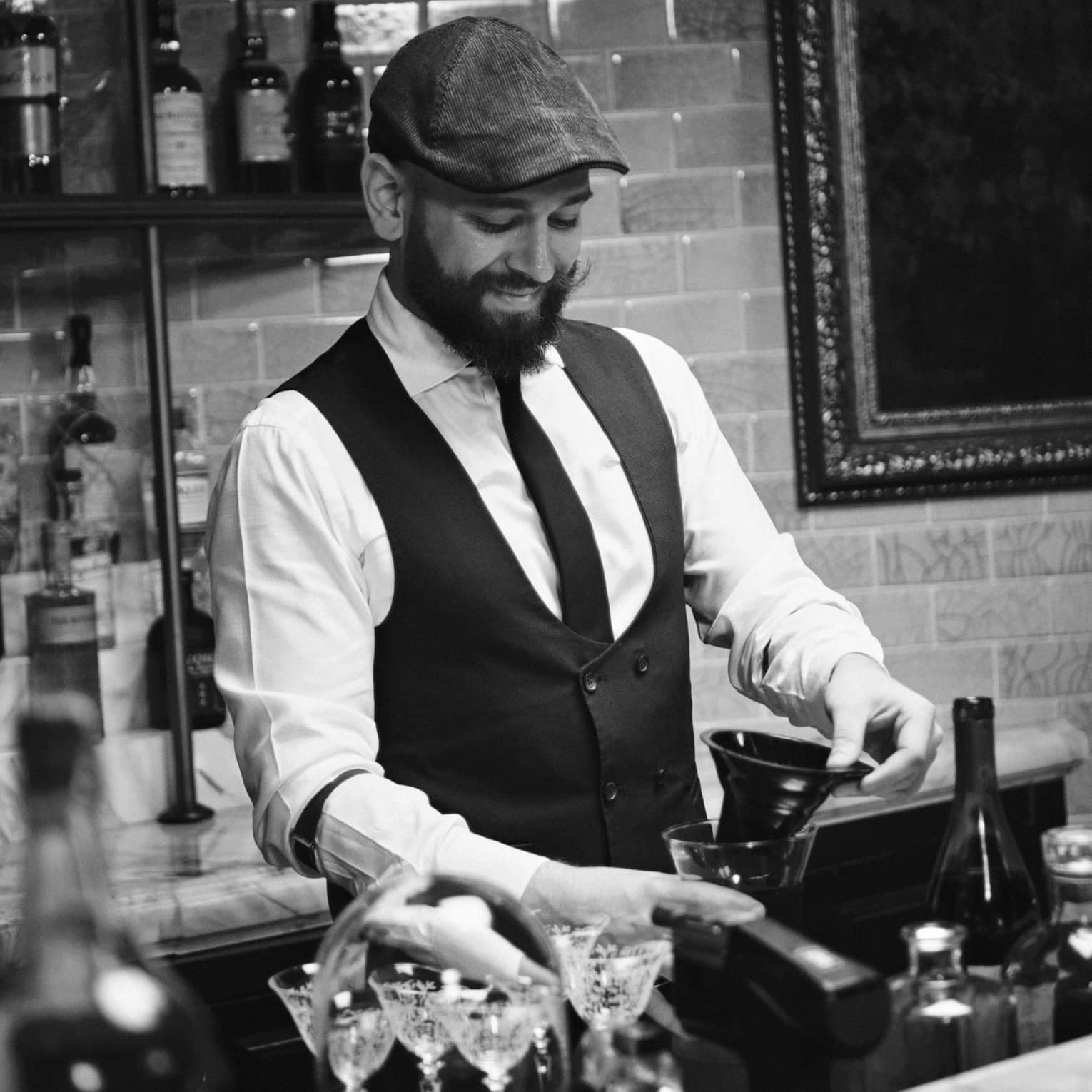 A bartender wearing a tie and vest works behind a bar
