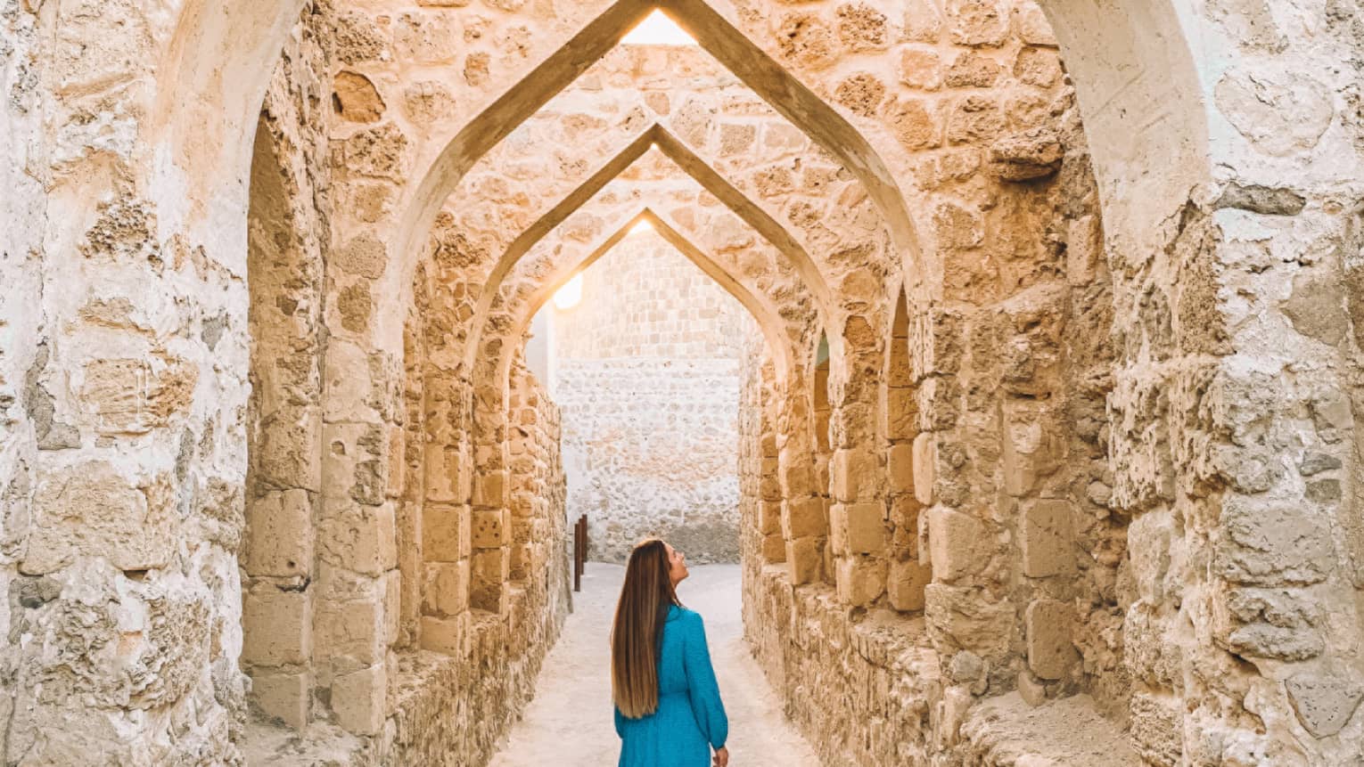 A woman stands underneath a stone pathway.