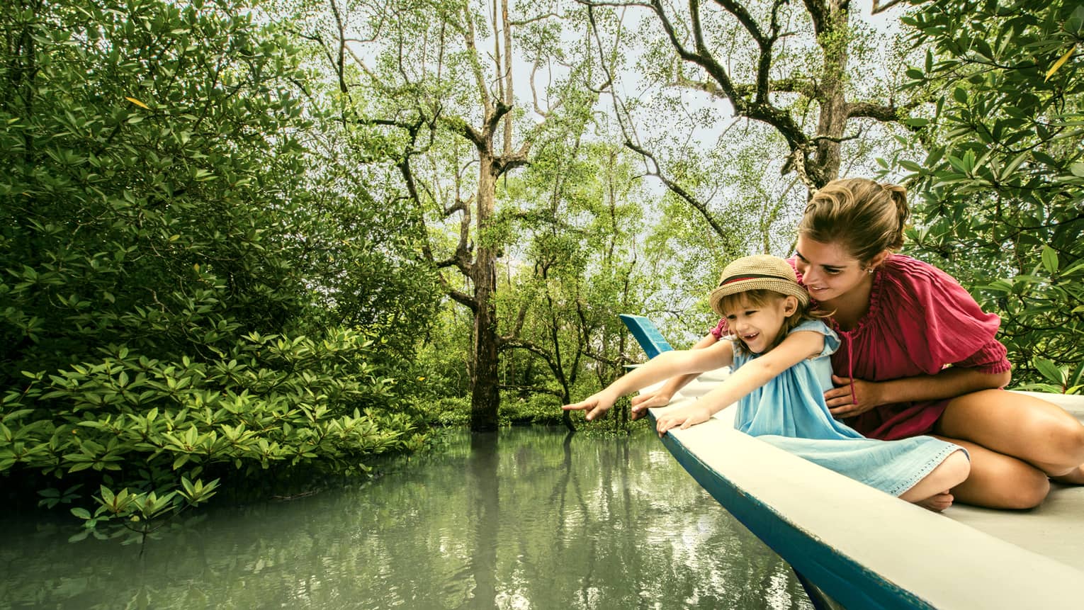 Mom, young daughter in back of wood canoe look into river