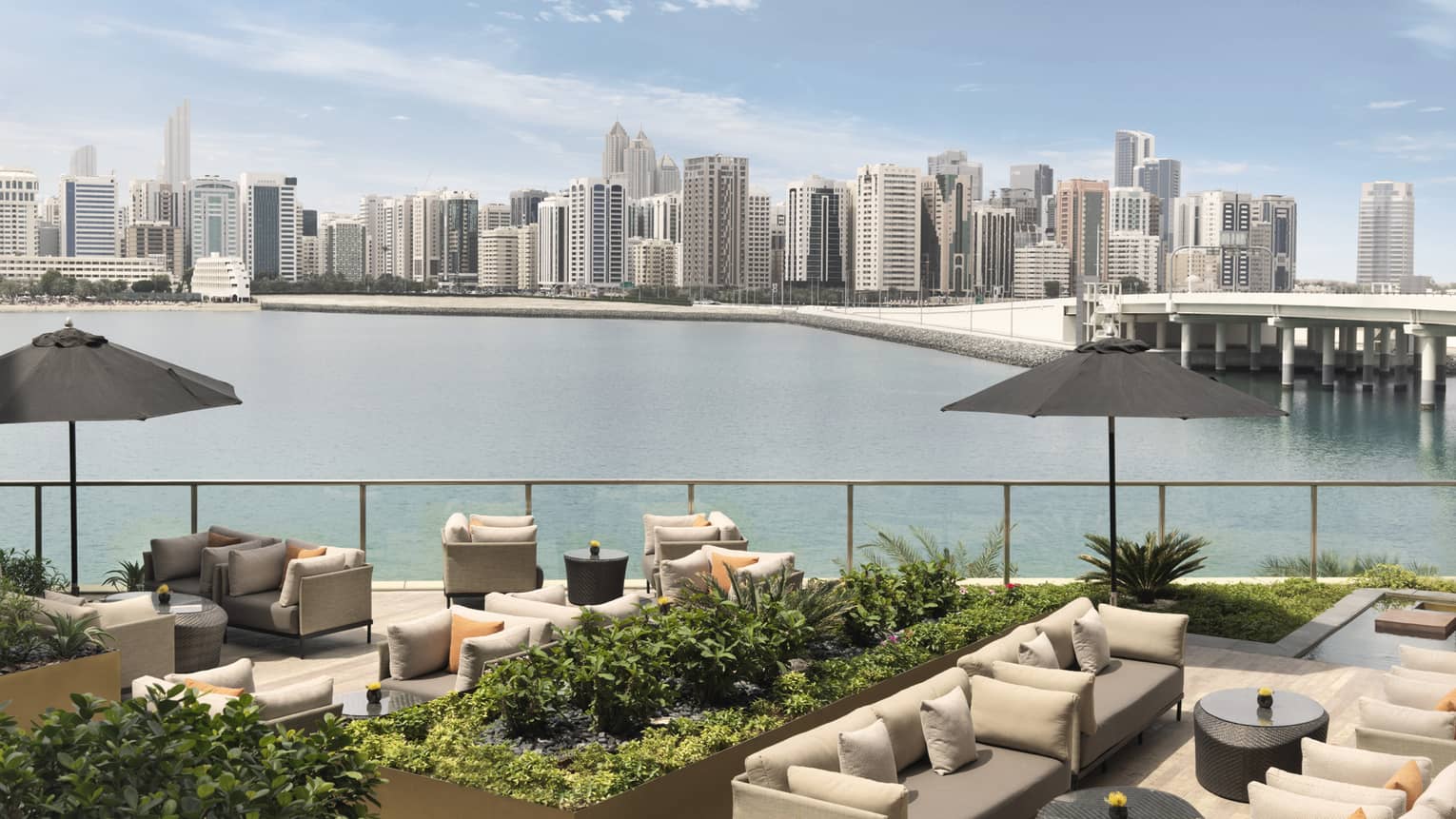 Outdoor sofas, umbrellas and planters on patio overlooking water, city