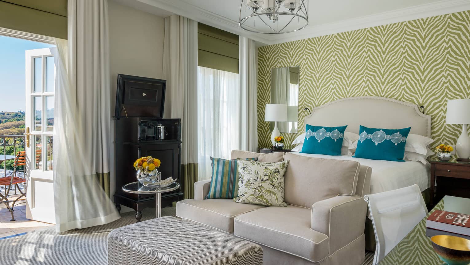 Panoramic View Deluxe Room white loveseat and ottoman against patterned wallpaper, open door to sunny patio