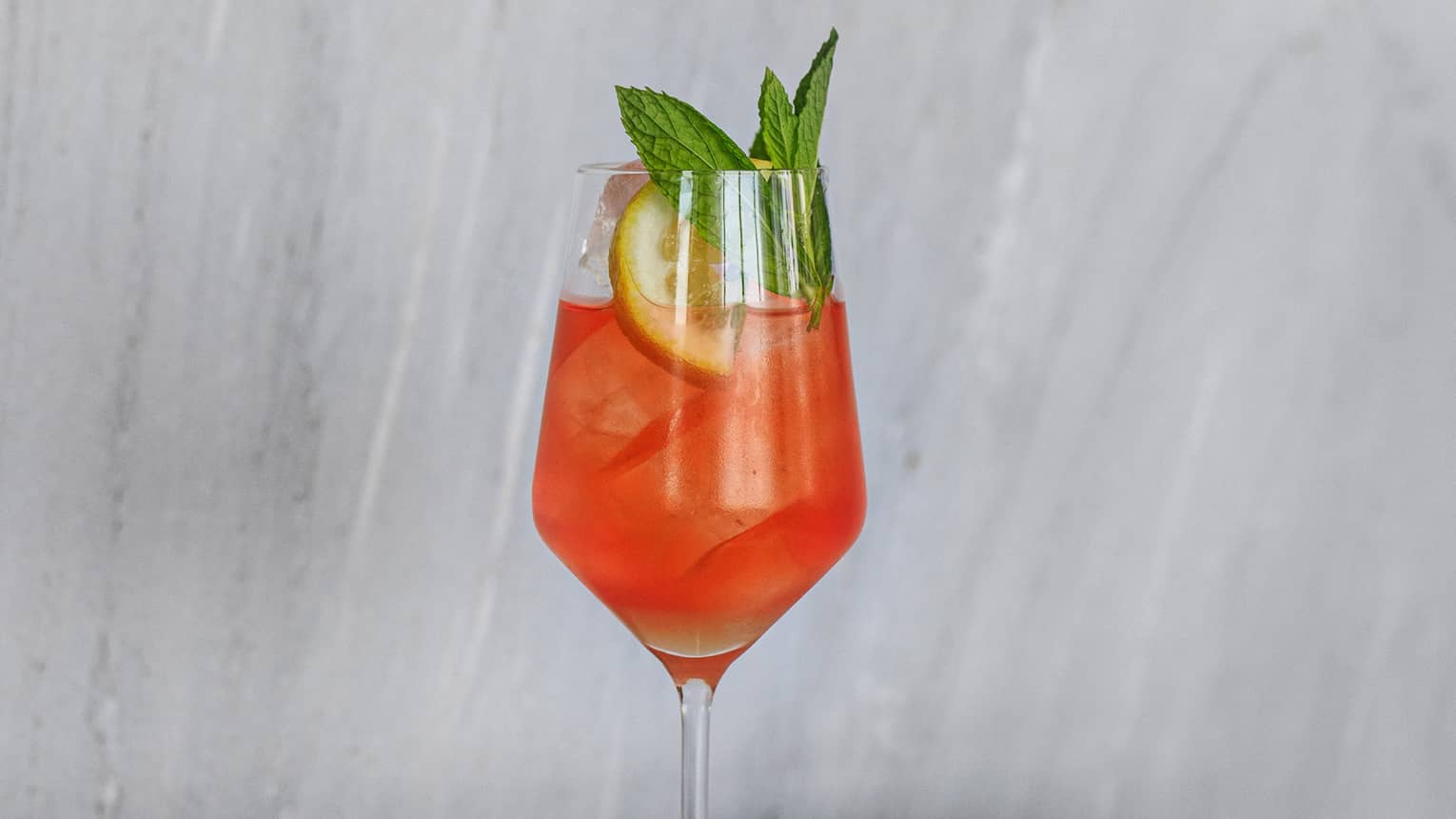 Caroli Spritz of Aperol, Lemon Sherbet, Brut Champagne in tall wine glass with fruit and mint garnish