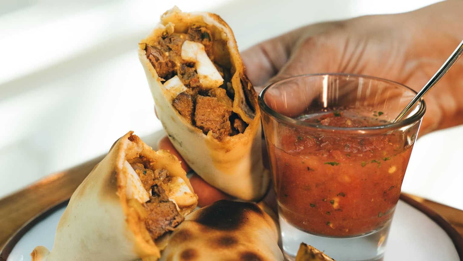 Two beef empanadas served on a round white dish with a small glass of dipping sauce