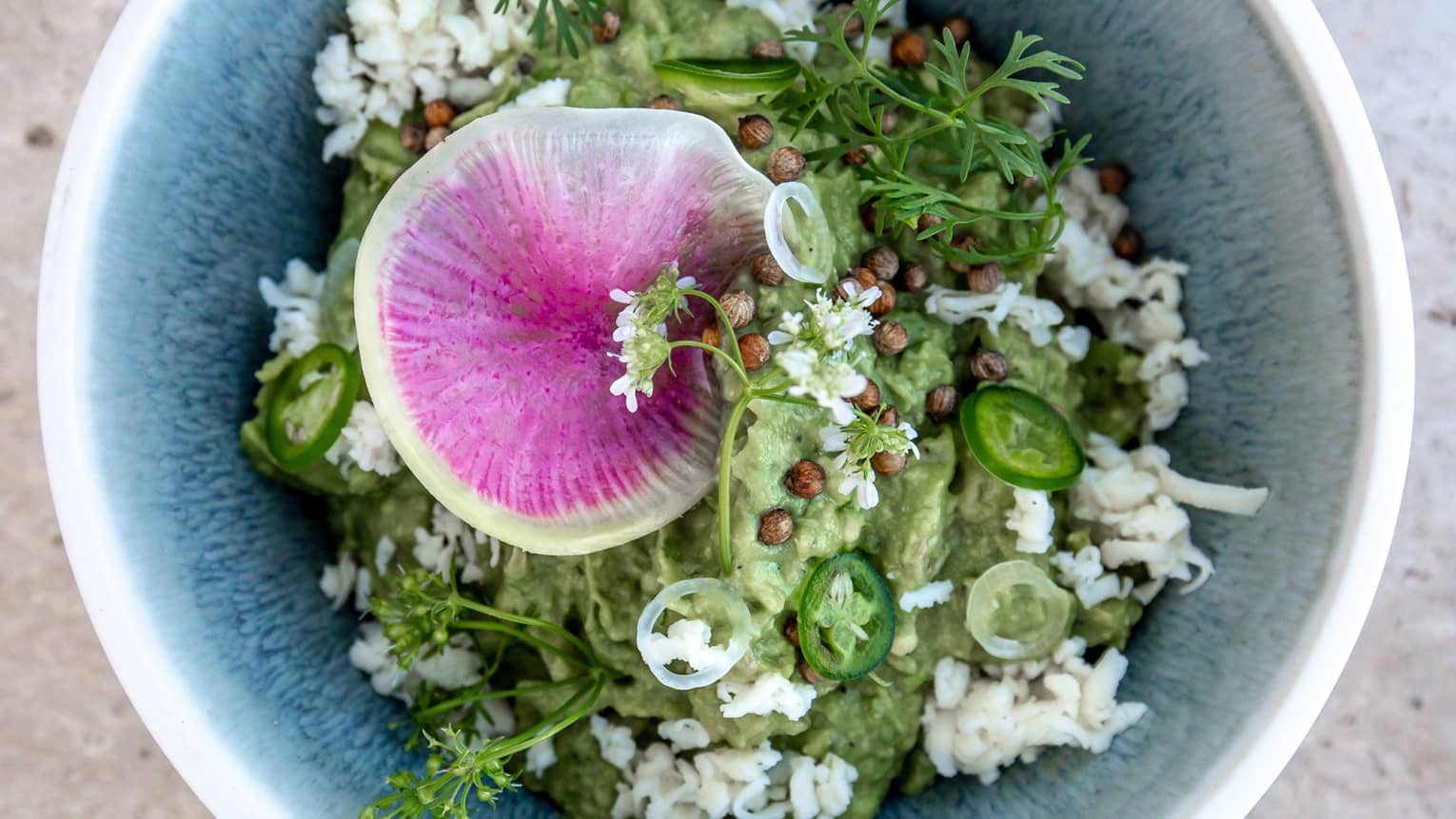 A blue bowl with herbs and guacamole in it.