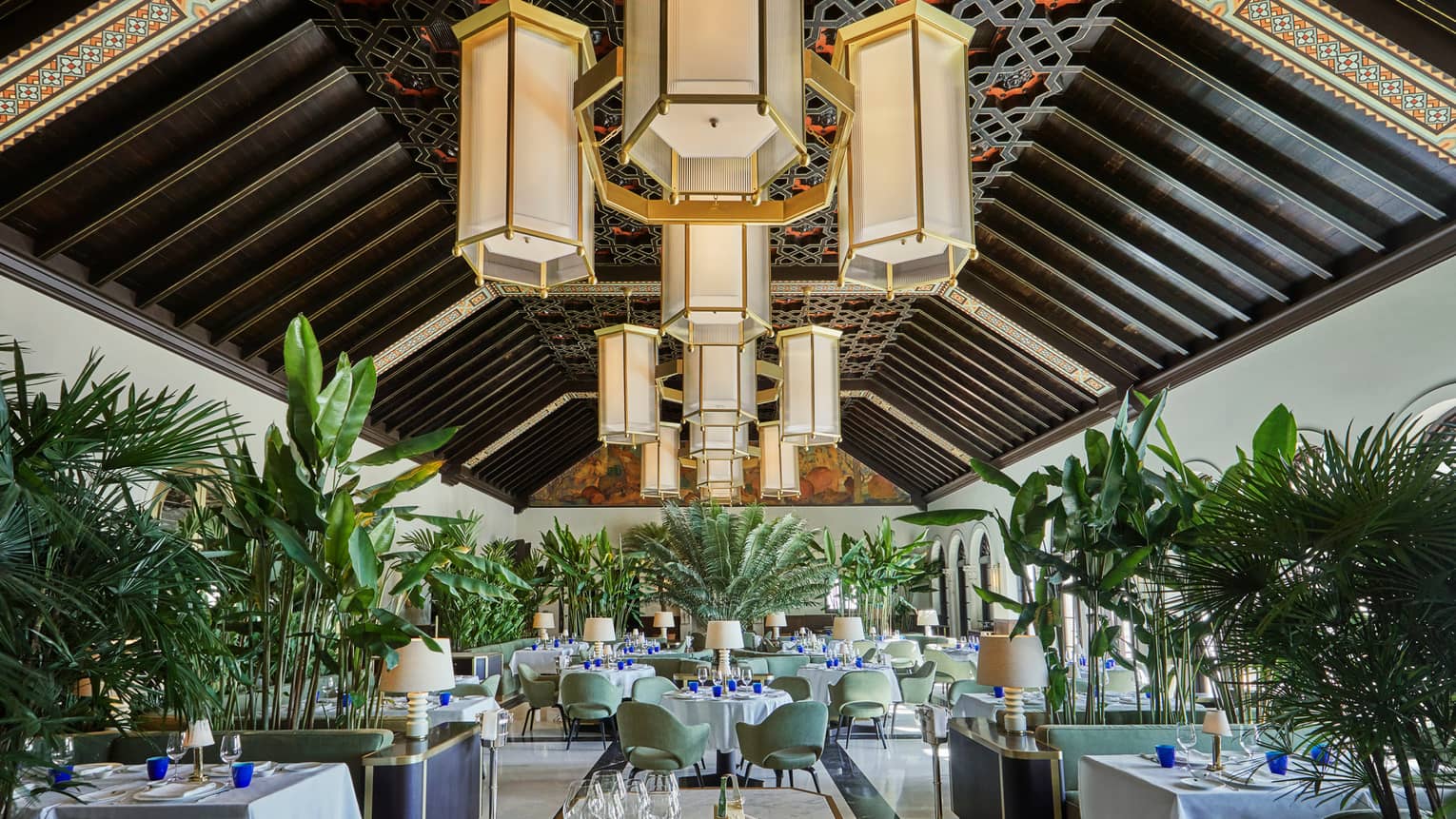 Historic Peacock Alley restored dining room with high ceilings, art deco-style chandeliers and tropical plants