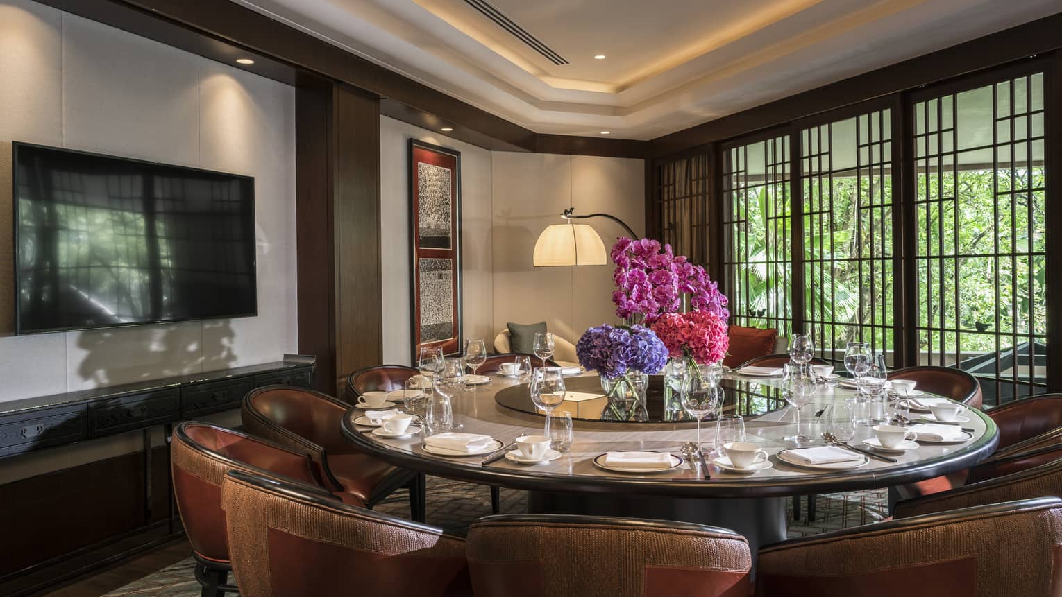 Round private dining meeting table with large pink floral display in centre, TV on wall