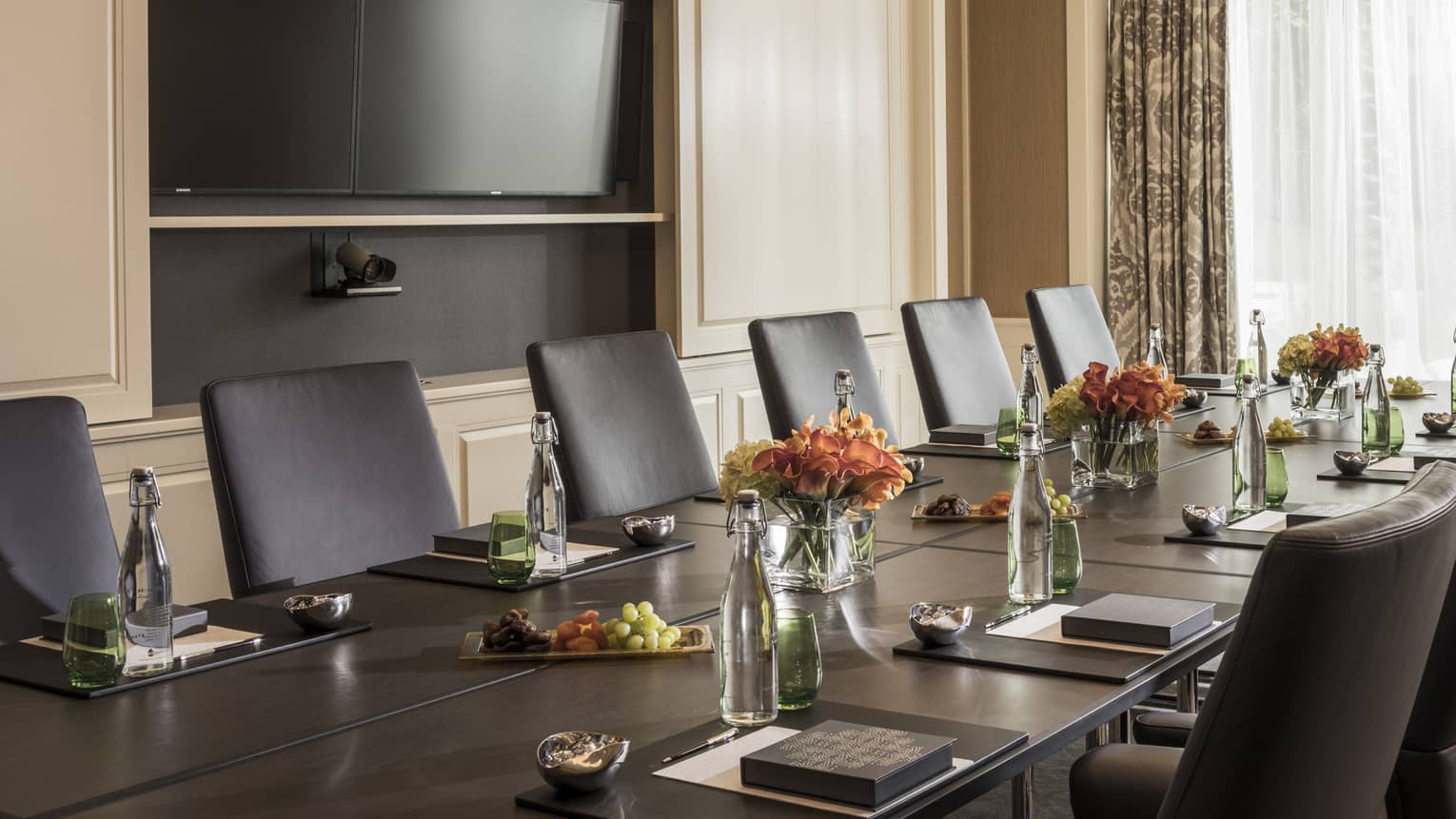 Long boardroom table set with glass bottles of water, flowers in bright meeting room