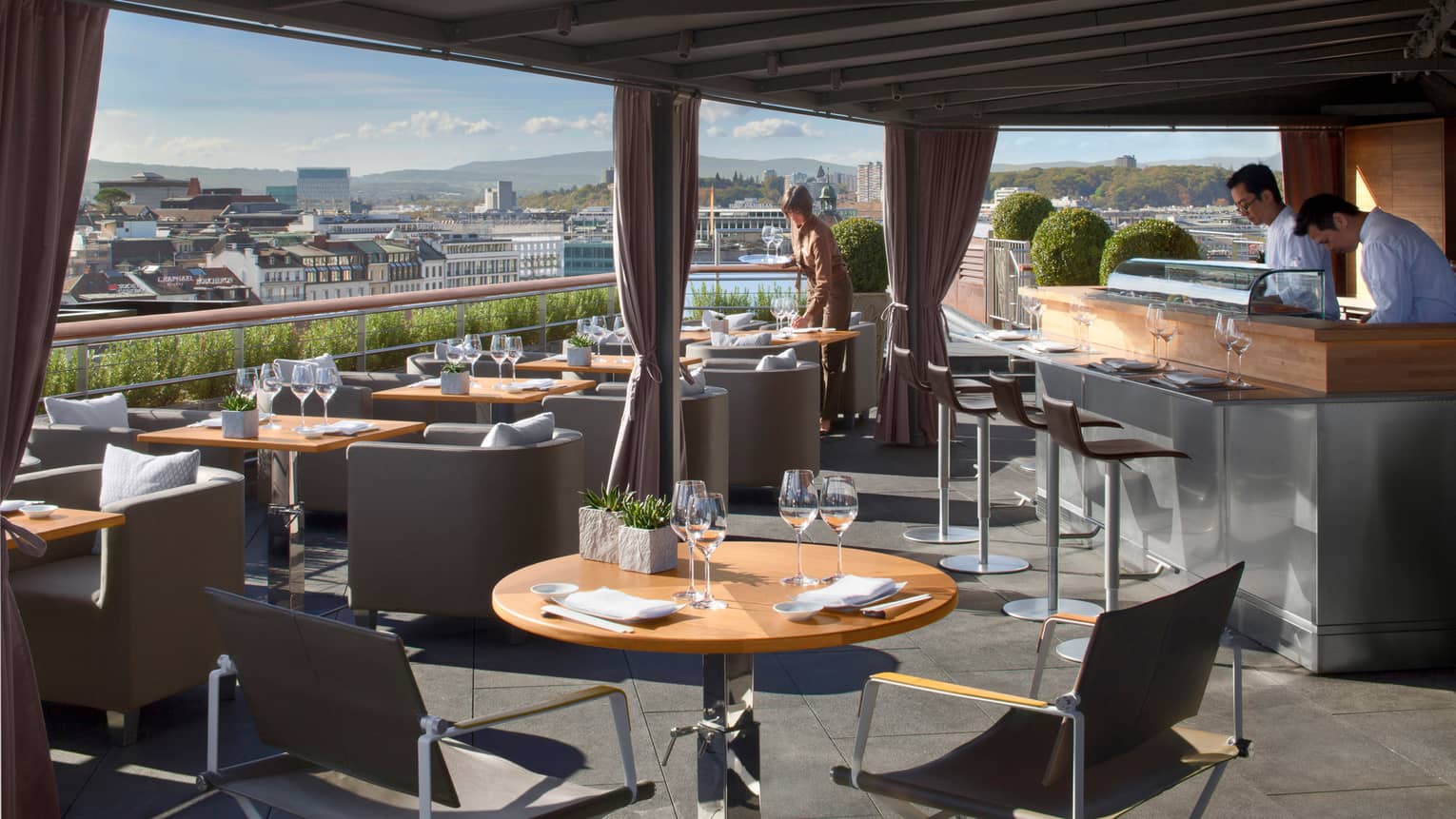 Feast on 360˚ rooftop patio dining tables and chairs under awning on sunny day, bartenders and server sets table