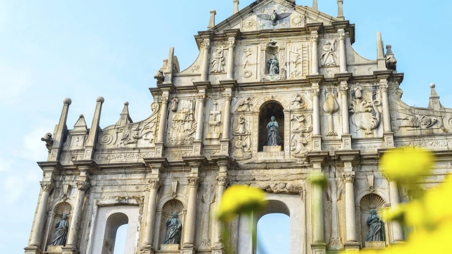 An ornate facade with archways at bottom, lined with thin towers and columns, intricate carvings and shelves holding statues.