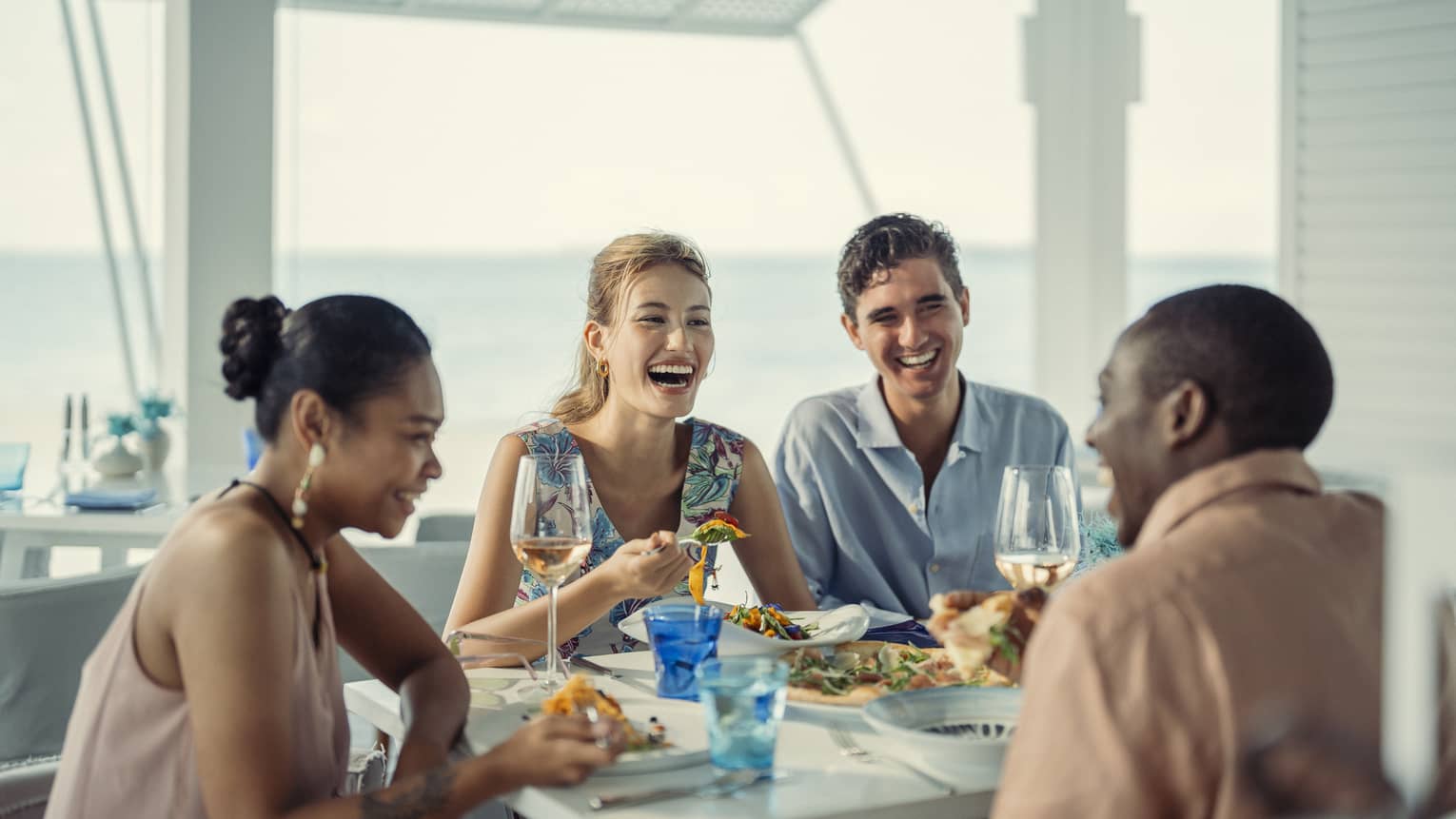 Two couples laugh over a meal at Blu Beach Club
