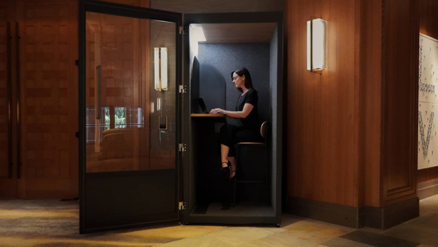 Woman sits in a glass-walled and sound-proofed virtual office room