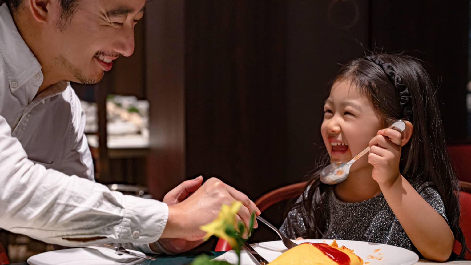 Smiling young girl and her dad dig into omurice topped with ketchup