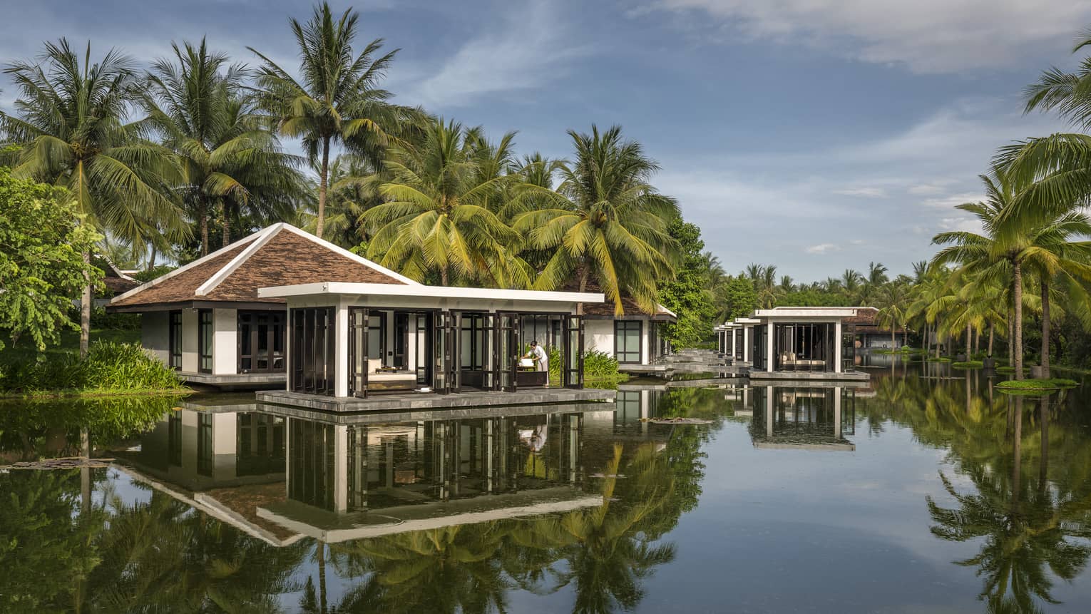 Overwater Heart of Earth spa villa staff folds white towels on deck, reflection in water