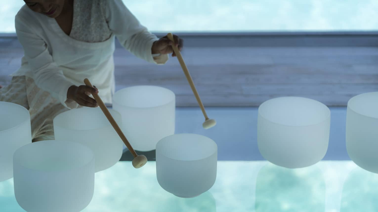 Spa staff plays various white crystal bowls with wood mallets during sound healing session