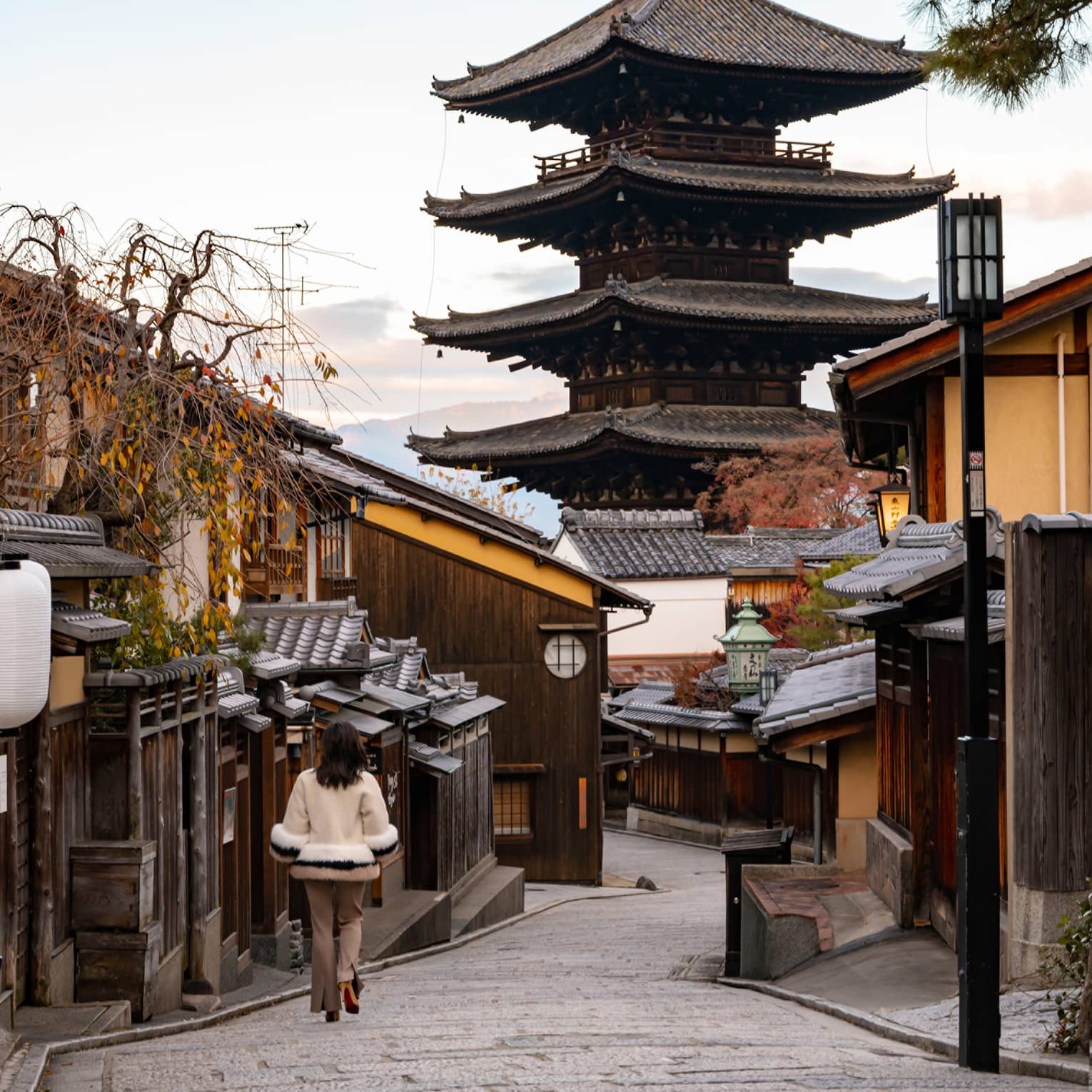 Woman walks down cobblestone street in Kyoto towards Japanese pagoda
