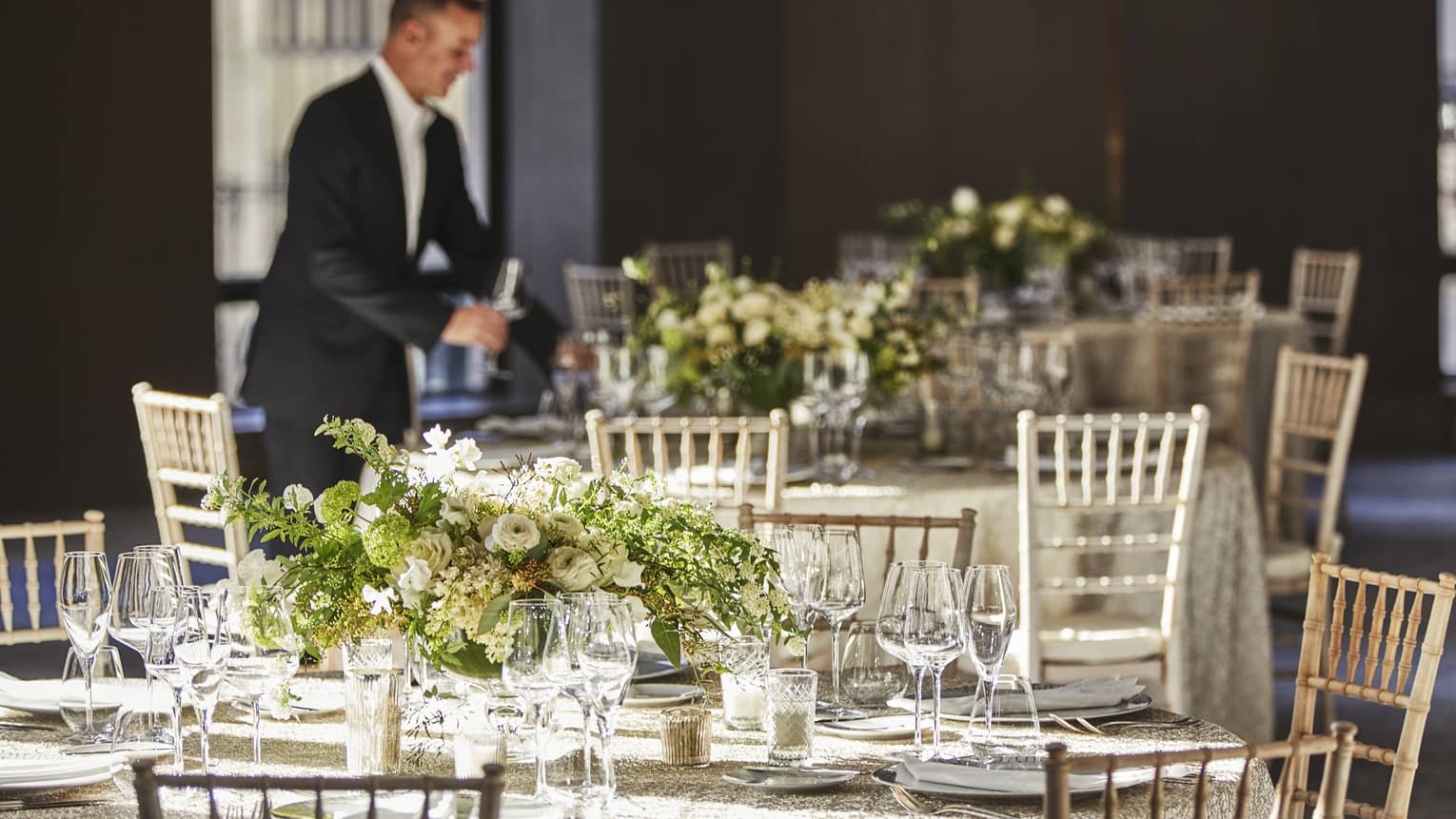Man wearing suit behind round wedding reception tables with white flowers