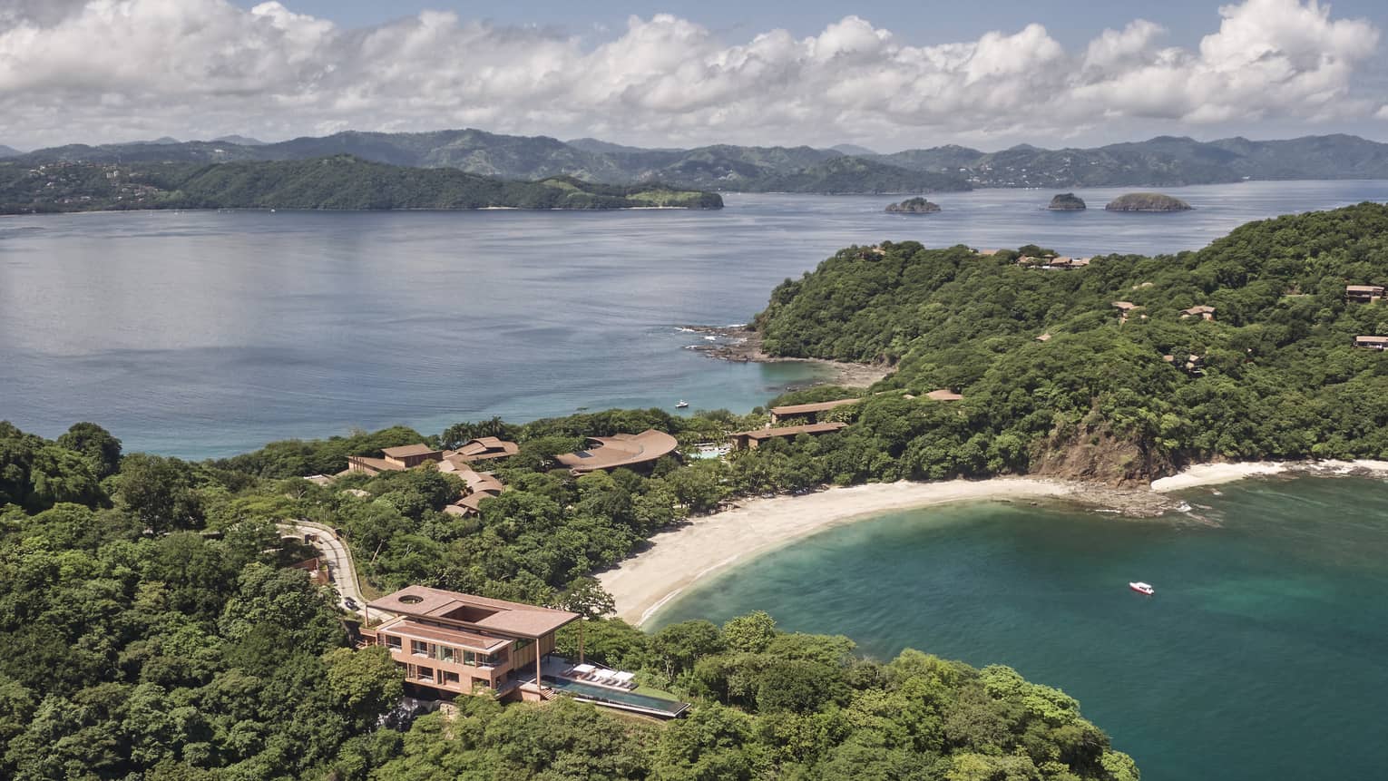Aerial view of a private villa surrounded by trees near a beach/bay
