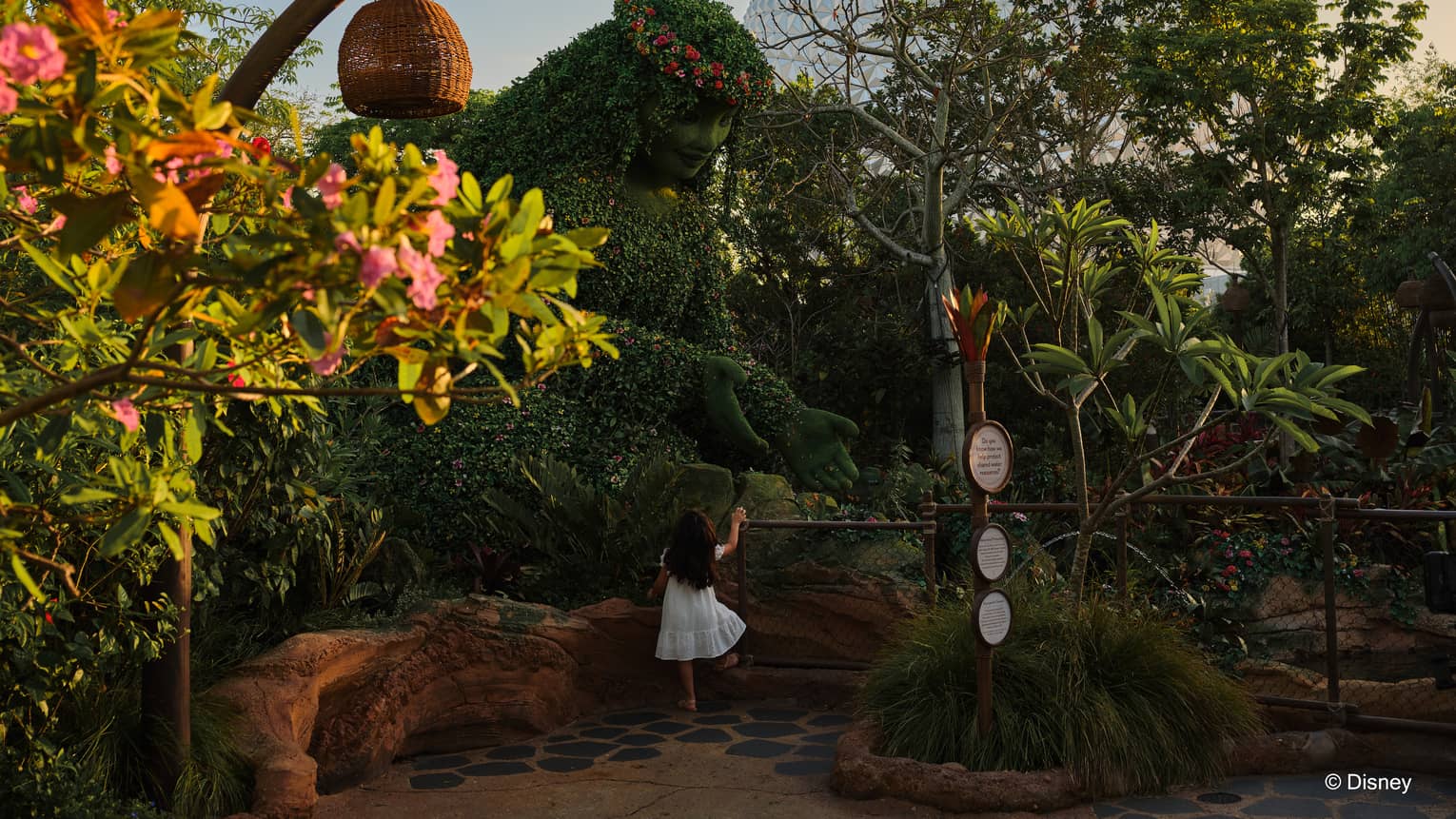 Child stand in front of a ledge of greenery at EPCOT with Spaceship Earth peaking over the trees