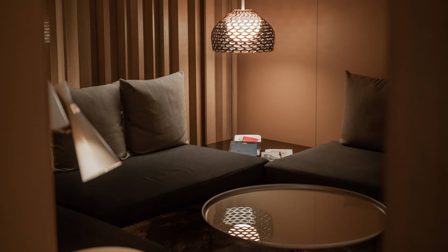 Corner of a modern spa lounge area with black couches, a circular, mirror-top coffee table and floor lamp