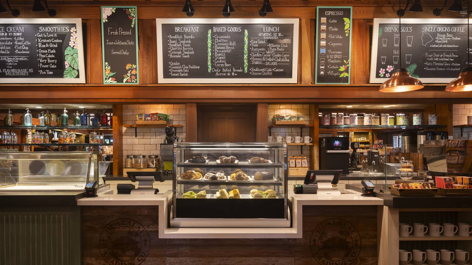 An eatery counter with menu boards overhead, stocked shelves behind it, and display cases and shelves on top of and in front of it