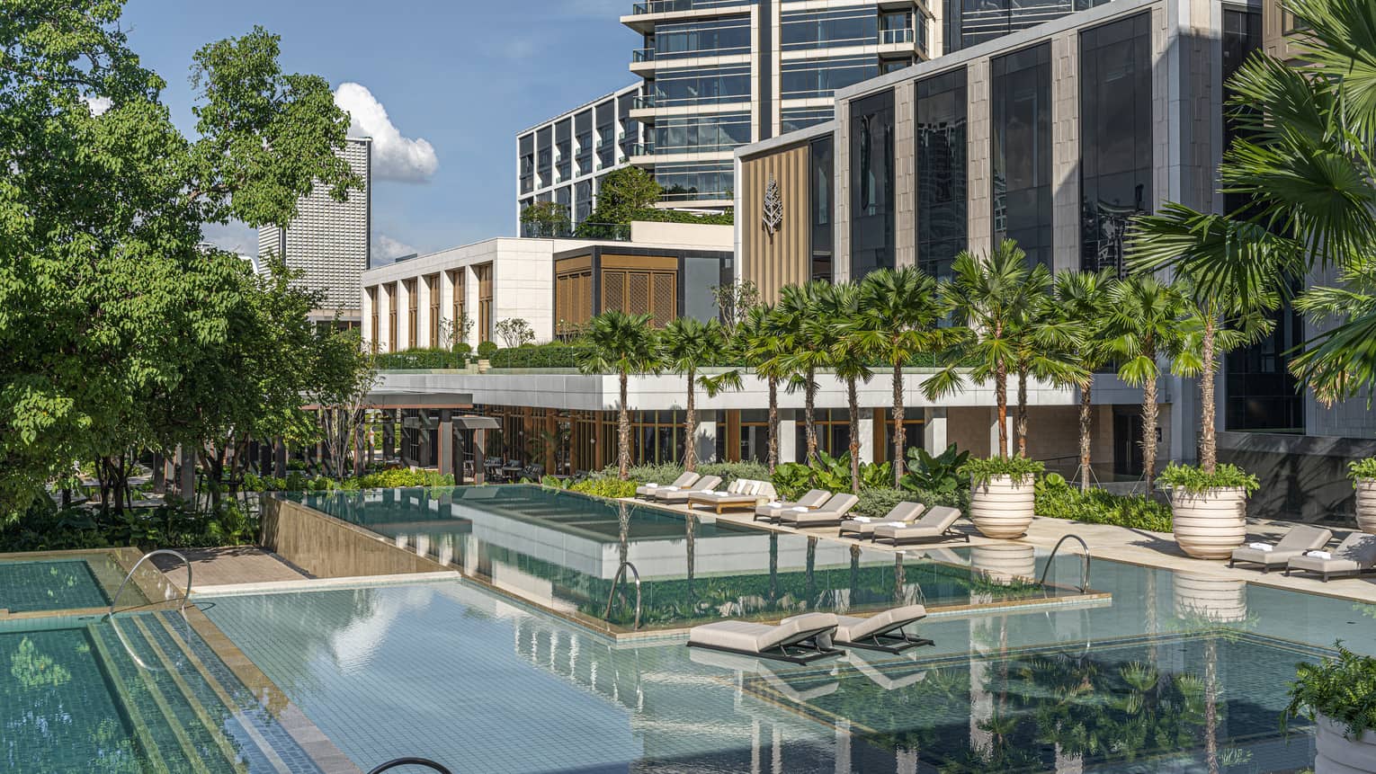Outdoor pool, lined with potted trees and lounge chairs, reflection of hotel building