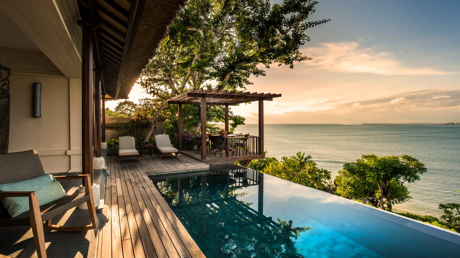 Private Ocean Villa patio at sunset with infinity swimming pool reflecting trees, clouds, white lounge chairs on side