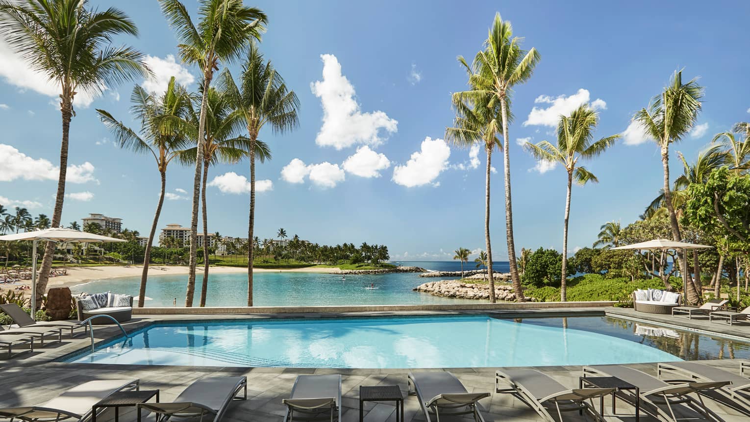 Sunny outdoor swimming pool lined with lounge chairs, palm trees