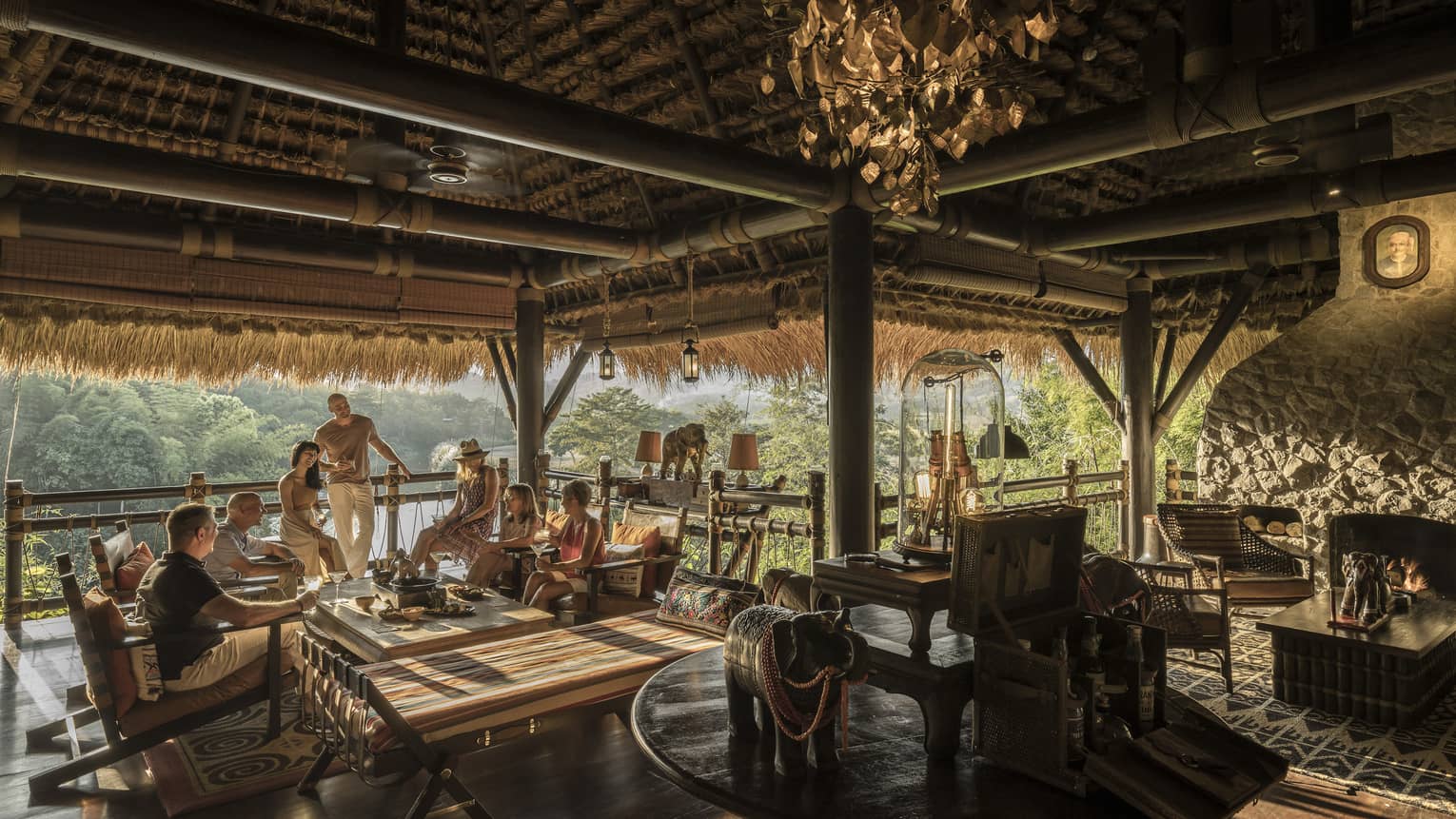 People mingle at open-air bar, beamed thatched roof, lounge seating, trees in the distance