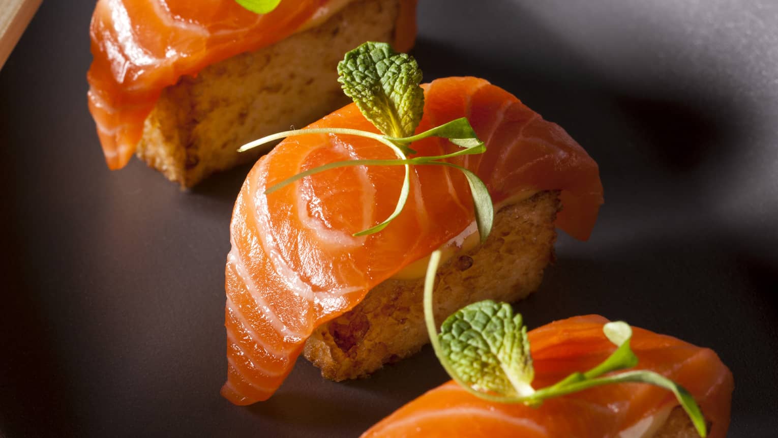 Three pieces of crispy salmon sushi on black platter