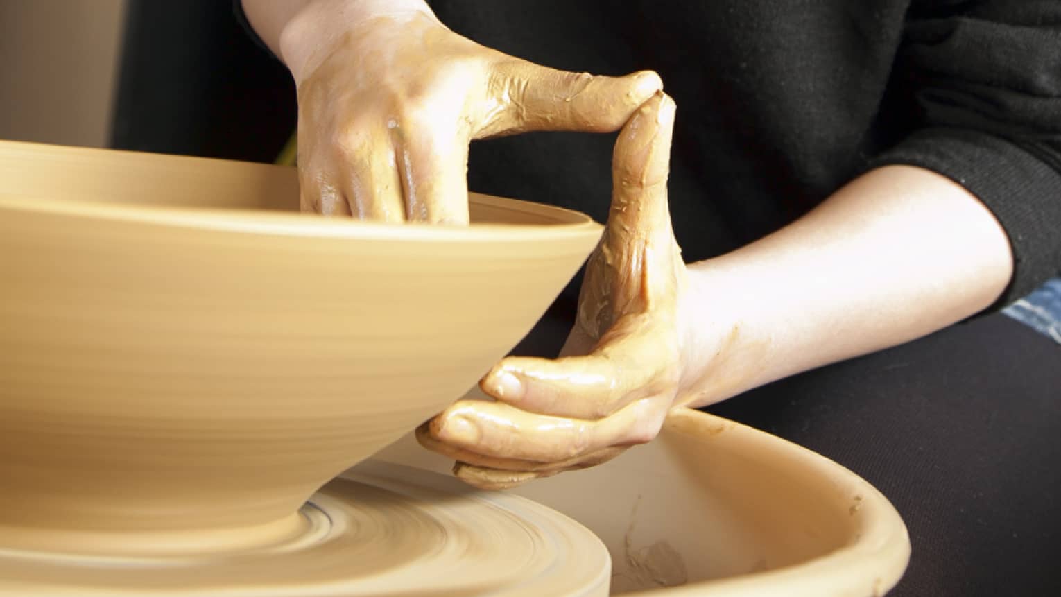 Woman makes clay bowl on pottery wheel