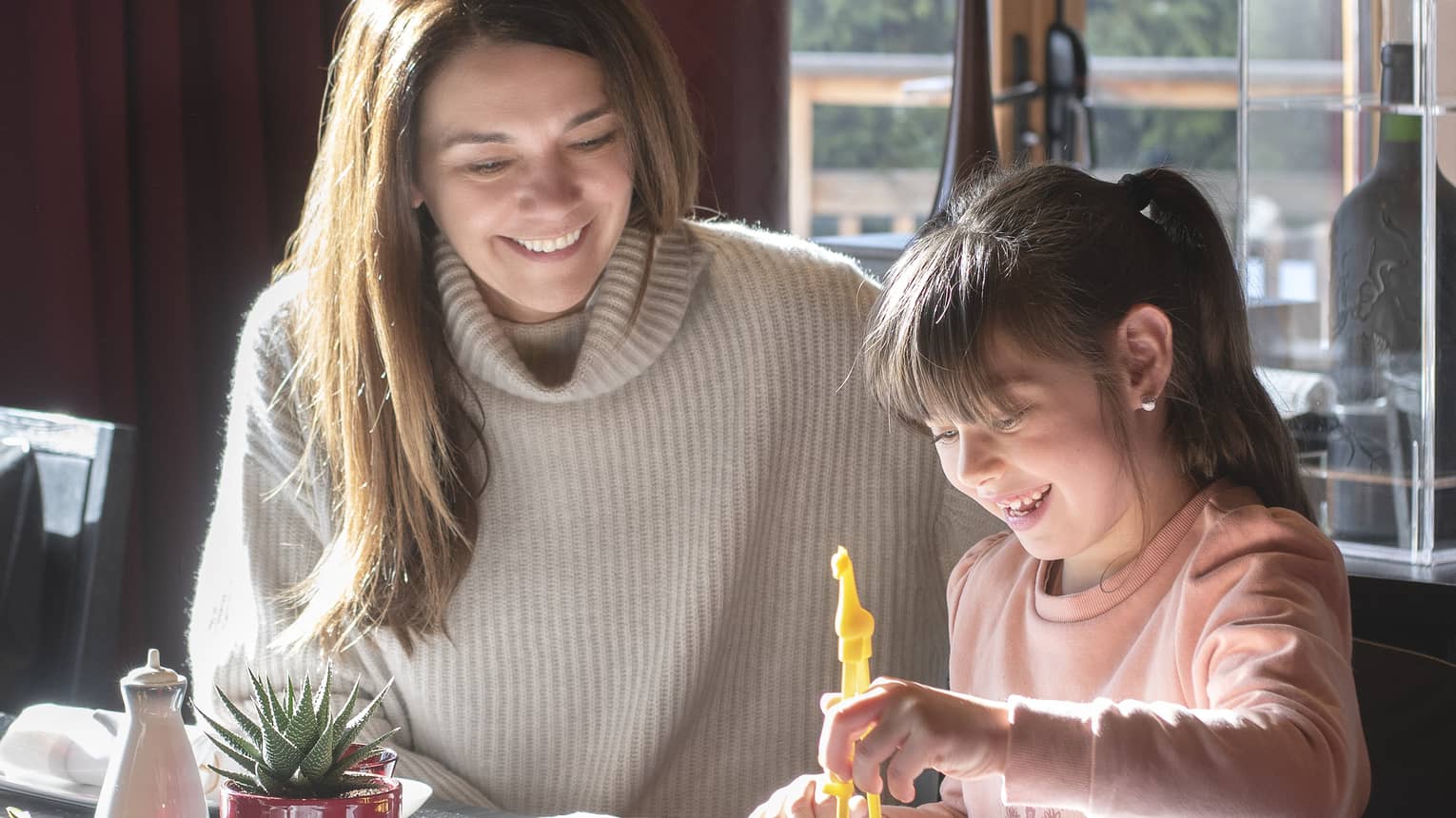 Mom and daughter smiling as daughter picks up sushi from bento box with chopsticks