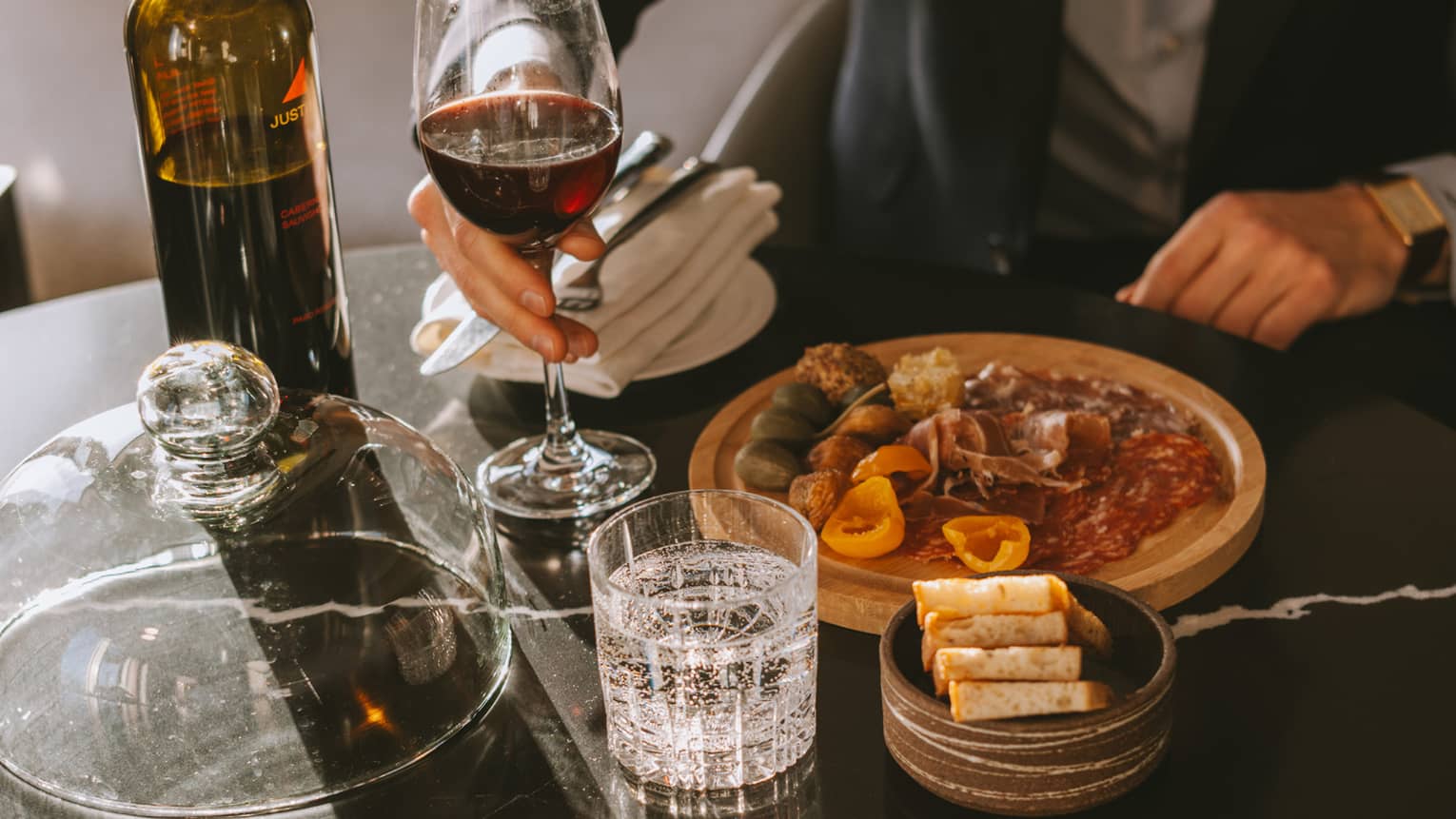 Man sits at a table with glass of red wine and charcuterie